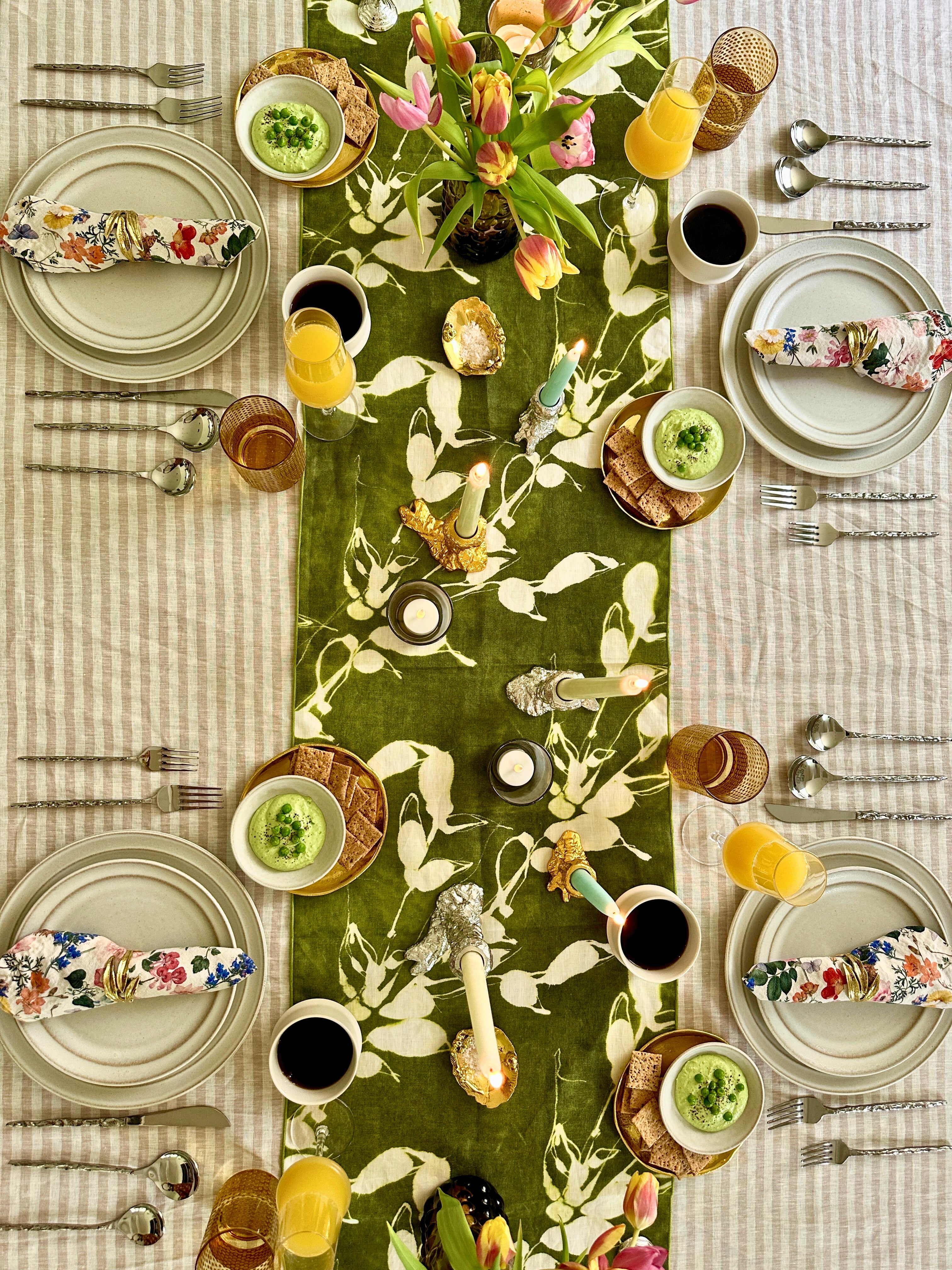 Dining table set with floral table runner, striped tablecloth, dining ware, and fresh flowers.